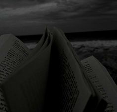 an open book sitting on top of a beach next to the ocean under a cloudy sky