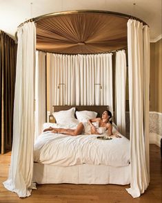 a woman laying on top of a white bed in a bedroom next to a window