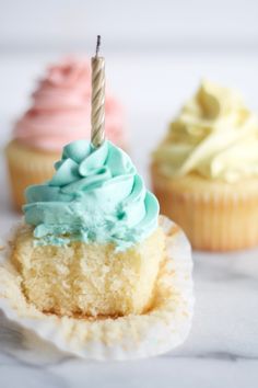 three cupcakes with frosting and a single candle sticking out of it's top