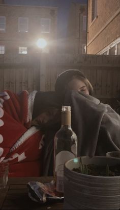 two people sitting on a couch with a bottle of wine in front of them and a light shining through the window