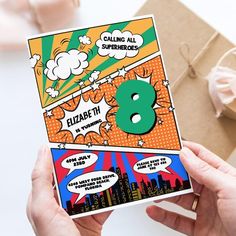 someone holding up a comic book with the number 8 on it and an envelope in front of them