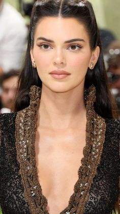 a woman with long dark hair wearing a black and gold dress on the catwalk