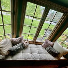 a window seat with pillows on it in front of some large windows and grass outside