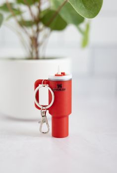 a red cup shaped keychain sitting on top of a white table next to a potted plant