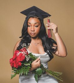 a woman wearing a graduation cap and gown holds flowers in her hand while posing for the camera