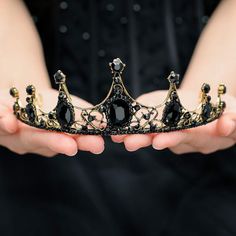 a woman is holding a black crown in her hands and it looks like she's wearing a tiara