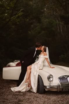 a bride and groom kissing in front of a classic car