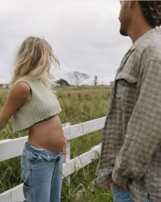 a pregnant woman standing next to a man near a fence