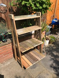 a wooden shelf sitting on top of a sidewalk next to a brick wall and potted plants