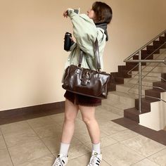 a woman holding a brown purse standing in front of a stair case and looking up