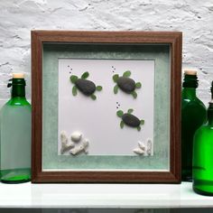 some green bottles are sitting on a shelf and there is a picture frame with two turtles in it