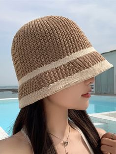 a woman standing next to a swimming pool wearing a brown and white knitted hat