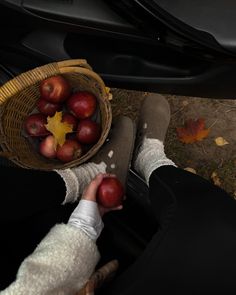 a person holding apples in their hands while sitting on the ground next to a car