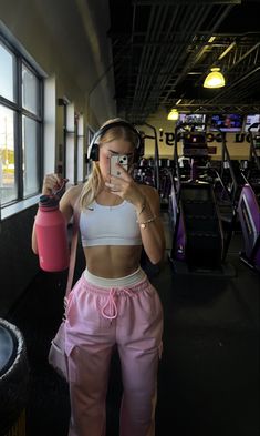 a woman taking a selfie in front of a gym mirror with headphones on