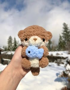 a hand holding a brown and white teddy bear with a blue pacifier in it's mouth