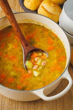 a wooden spoon in a pot filled with soup next to rolls and bread on the table