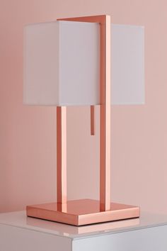 a lamp that is sitting on top of a white table next to a pink wall