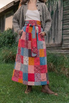 a woman standing in front of a barn wearing a multicolored patchwork skirt