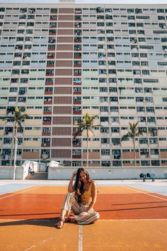 a woman sitting on top of a tennis court next to a tall building with balconies