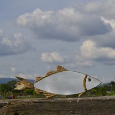 a fish shaped mirror sitting on top of a wooden fence