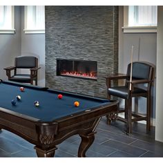 a pool table with balls on it in front of a fire place and two chairs