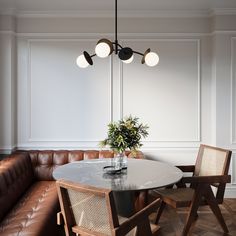 a dining room table with chairs and a vase on the top, in front of a brown leather couch