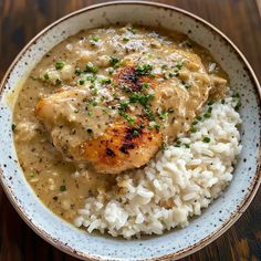 a bowl filled with rice and chicken covered in gravy on top of a wooden table