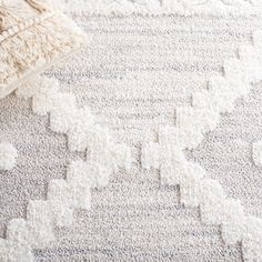 an area rug with white and gray designs on the floor, next to a pillow