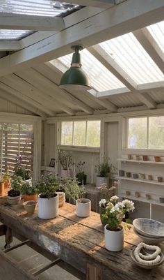 a wooden table topped with potted plants under a skylight in a room filled with windows