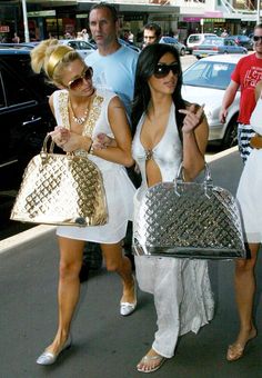 two beautiful women walking down the street carrying purses and handbags on their backs