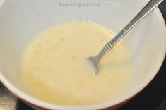 a white bowl filled with yellow liquid and a silver spoon in the middle, on top of a black surface