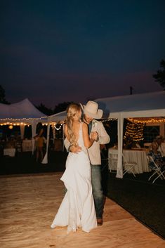 a bride and groom dance on the dance floor in front of their tent at night