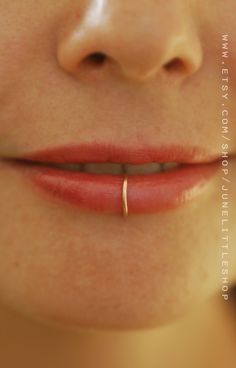 a close up view of a woman's mouth with a gold nose ring