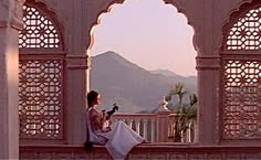 a woman is sitting on a wall and looking at her cell phone in the distance