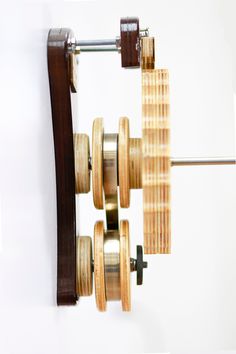 a wooden clock hanging from the side of a wall next to a metal bar with wheels on it