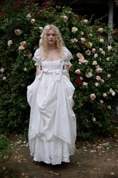 a woman wearing a white dress standing in front of flowers