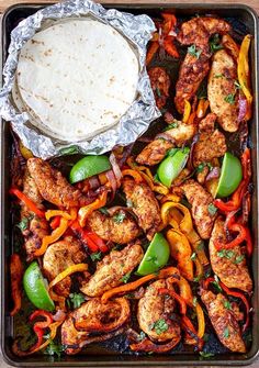 a tray filled with chicken and peppers next to a tortilla covered in sauce