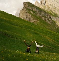 two people are playing in the grass with their hands up and one person is falling