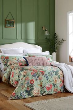 a bedroom with green painted walls and floral bed linens on the bed, along with a white headboard