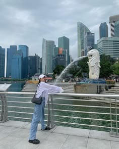 a woman standing next to a metal railing near a body of water with buildings in the background