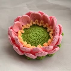 a crocheted pink and green flower sitting on top of a white table cloth