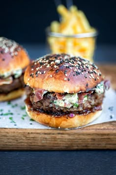 two burgers on a cutting board with fries in the background and text that reads blue cheese burgers on light broiled rolls / crispy panetta & onion chute