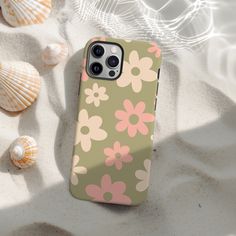 an iphone case with flowers on it sitting in the sand next to shells and seashells