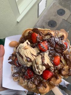 a waffle topped with ice cream, strawberries and chocolate sauce on a white plate