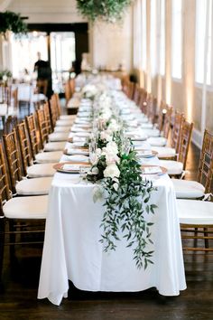 the long table is set with white linens and greenery