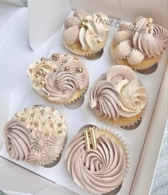 six cupcakes with frosting and gold decorations in a white gift box on top of a table