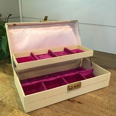 an open white box with pink velvet inside on a wooden floor next to a potted plant