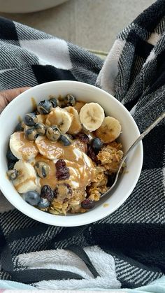 a person holding a bowl of cereal with bananas and blueberries