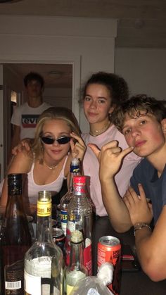 three people sitting at a table with bottles and drinks in front of them, posing for the camera