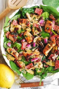 a salad with meat, onions and spinach on a white plate next to a lemon